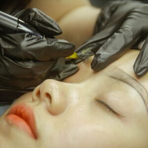 A detailed view of eyebrow microblading procedure with gloved hands and closed eyes.
